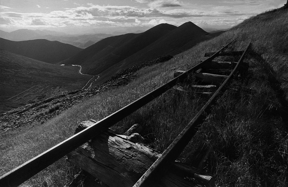Schwarz-Weiß-Fotografie einer Berglandschaft mit alten Schienen